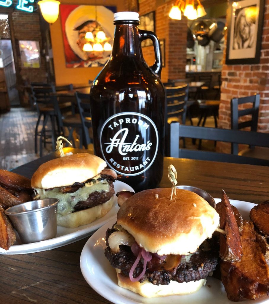 Two burgers with fries, Anton's Taproom bottle behind them