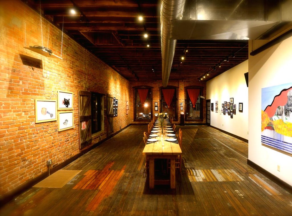 Anton's Taproom with long table, wooden chairs, large windows looking at street below, artwork on display